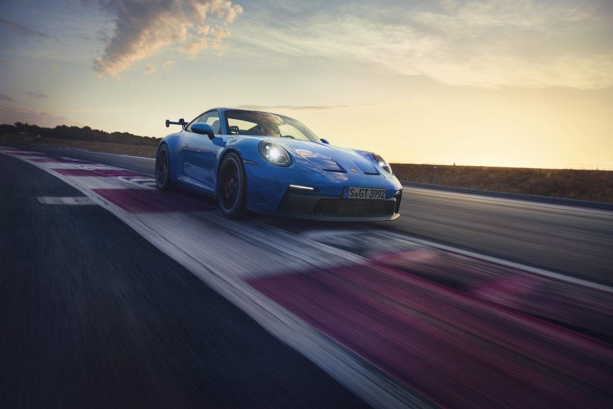 Vista frontale di 3/4 di una Porsche 911 GT3 blu del 2022 che gira in pista con il tramonto sullo sfondo.