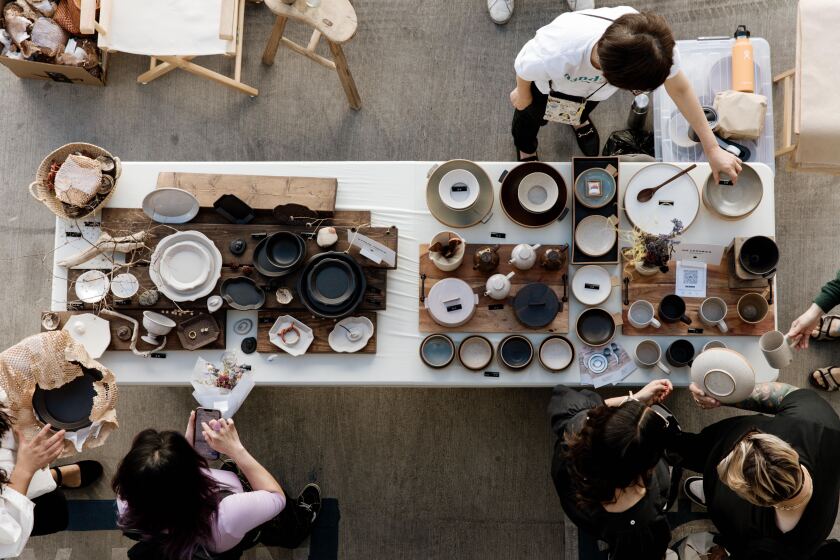 Immagine dall'alto di acquirenti che riempiono un tavolo di piatti, piatti, tazze e teiere in ceramica.