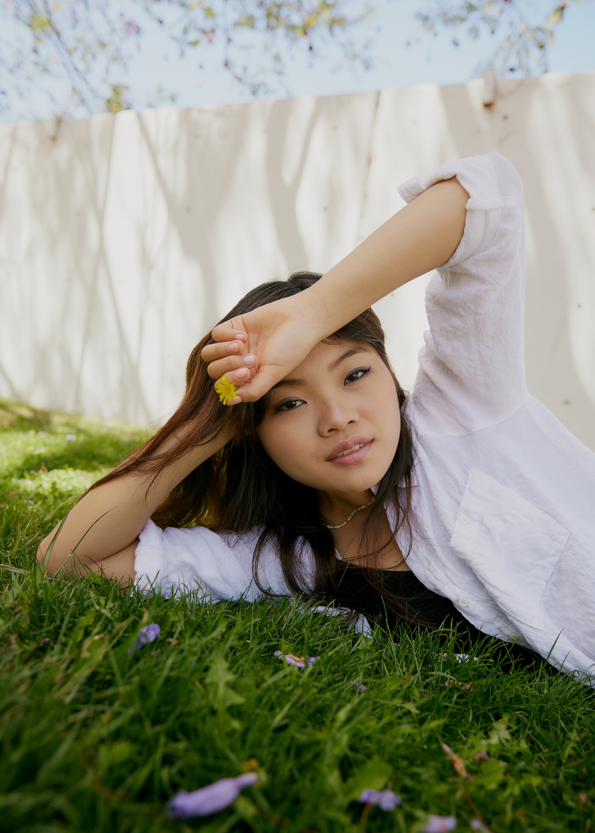 Mia Cheek è sdraiata sull'erba con in mano un piccolo fiore giallo.